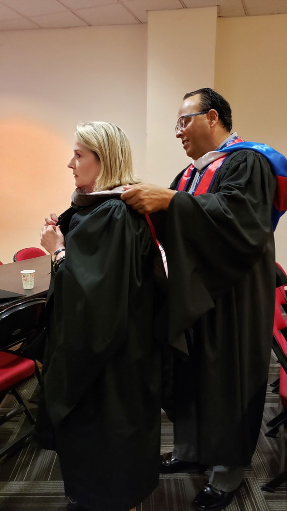 Department of Art and Design Chair Martin Valencia assists Holly Sowles with her hood as they prepare for commencement.