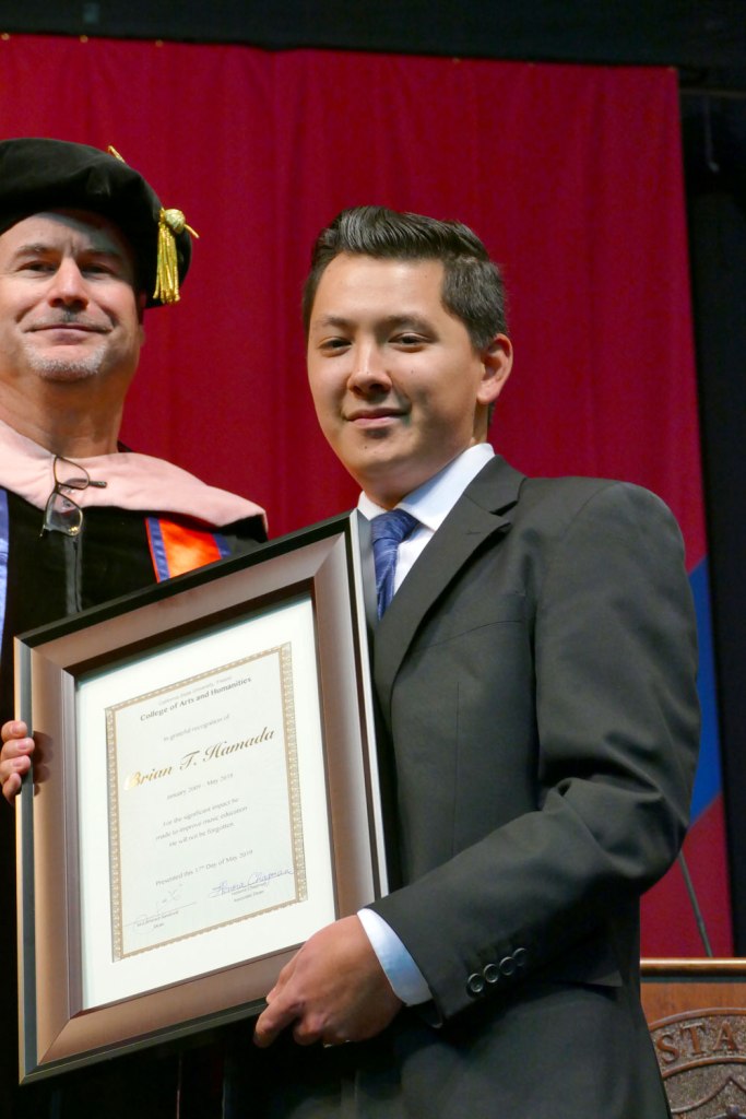 Evan Hamada accepts his father's Bachelor of Science degree Special Major: Music Management posthumously for his father Brian T. Hamada.