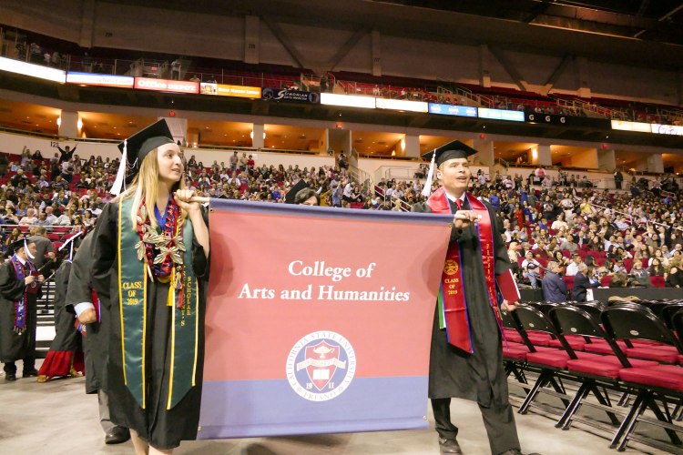 Standard Bearers Theresa Lopes and George Garnica lead the College of Arts and Humanities students.
