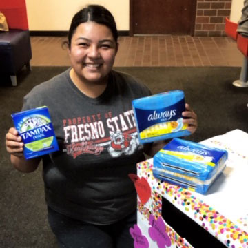 Student Giselle Hernandez hold mensuration products next to a donation bin.