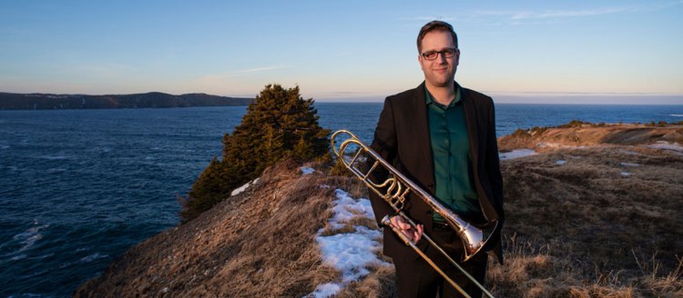 Dr. Stephen Ivany stands in front of an ocean bay holding his trombone.