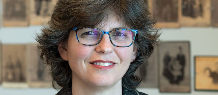 Dr. Zeynep Devrim Gürsel stands in front of a wall of faded photographs