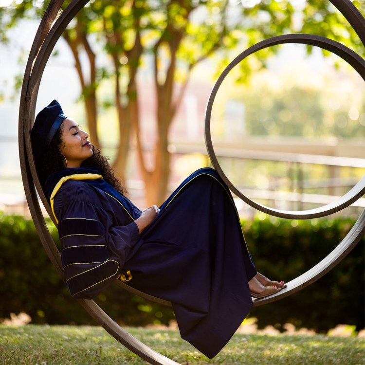 Alumna Kaelyn Rodríguez reclines inside a circular piece of outdoor art