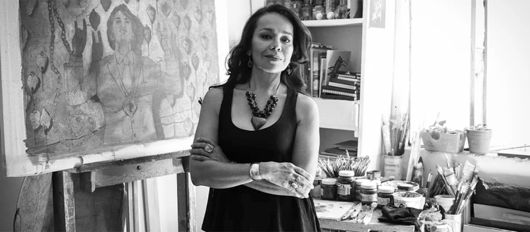 Rocío Caballero stands in front of her desk and a painting in her studio