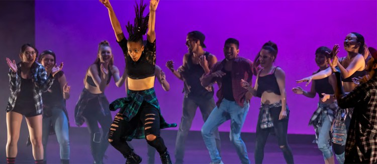 Dancer jumps on stage in front of other performers on the stage.