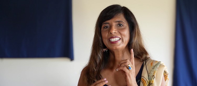 Dr. Veena Howard delivers her TEDx talk virtually in a cream colored room with two blue backdrops.