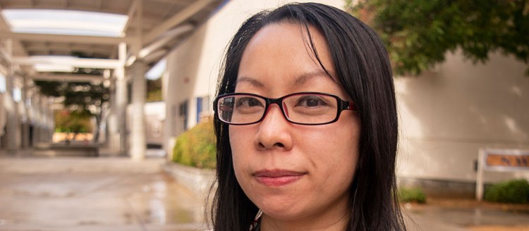 Lor Maiyang is seen in an open area with trees behind her, inside a school