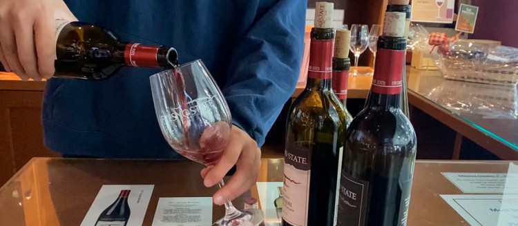 Fresno State red wine being poured into a class while four other bottles sit on the counter.