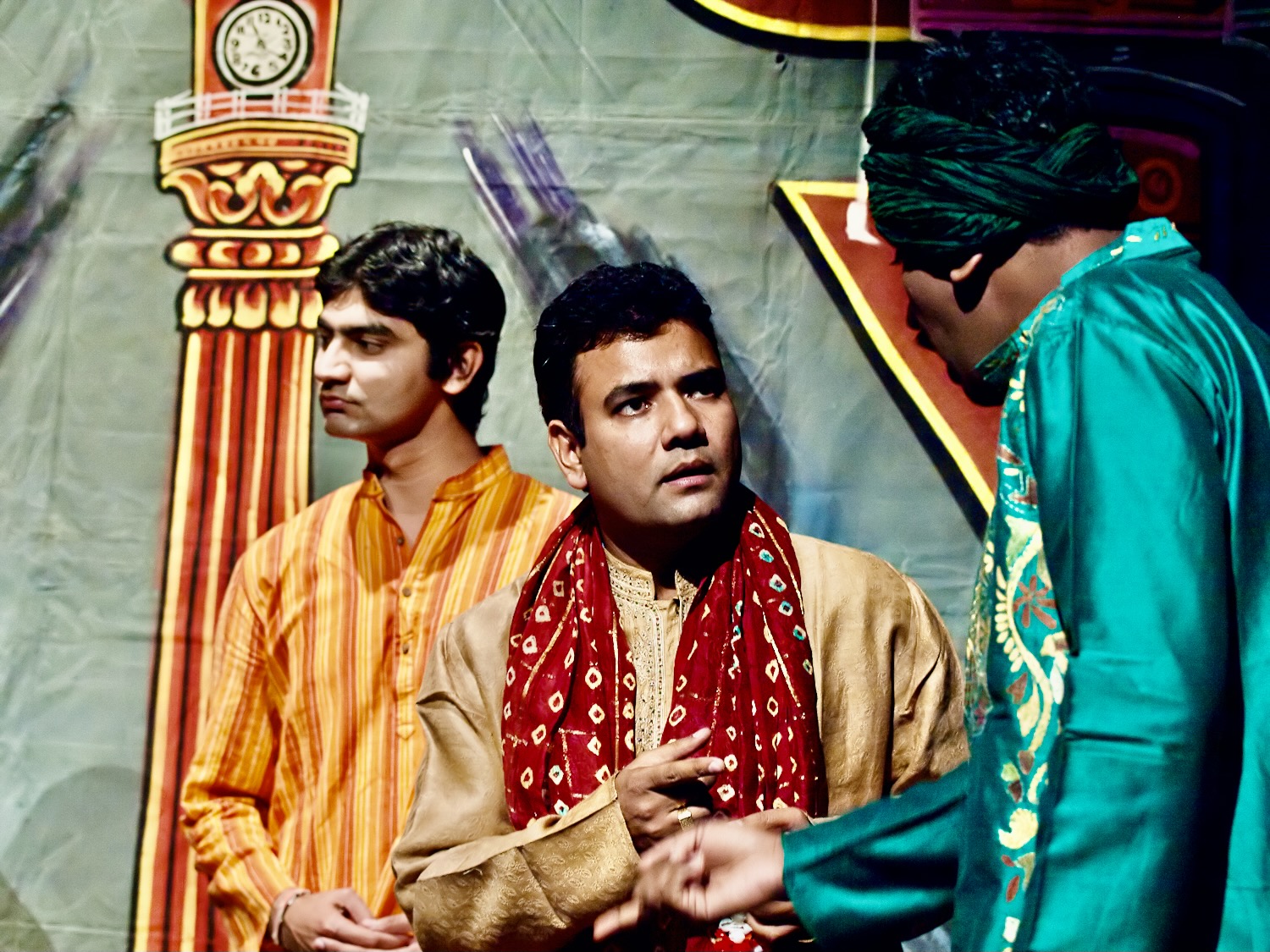 Dr. Devendra Sharma wears a traditional nautanki -- a gold shirt trims in lace with a red scare. He speaks with two other men in a wedding scene.