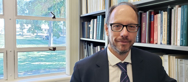Dr. Sergio LaPorta in next to his office bookshelf and his office window.