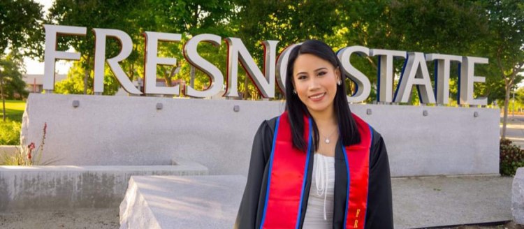 Diana Tinio stands in front of the Fresno State entrance sign in her graduation regalia.