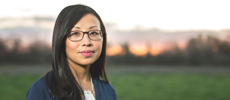 Finalist for the Pulitzer Prize in Poetry Mai Der Vang stands in front of a green field and a setting sun.
