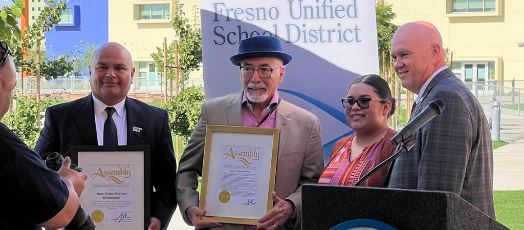 Juan Felipe Herrera poses with several dignitaries and framed declarations.