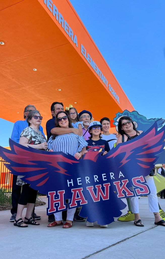 Juan Felipe Herrera poses with the Herrera Hawks logo and members of his family.