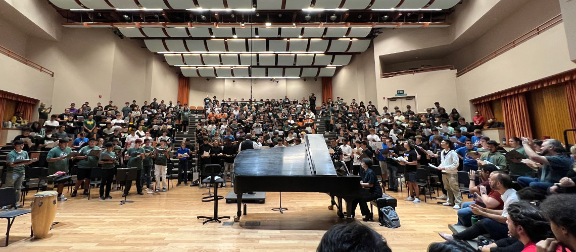 Over 300 high school students sing from the stands in the Concert Hall with piano accompaniment.