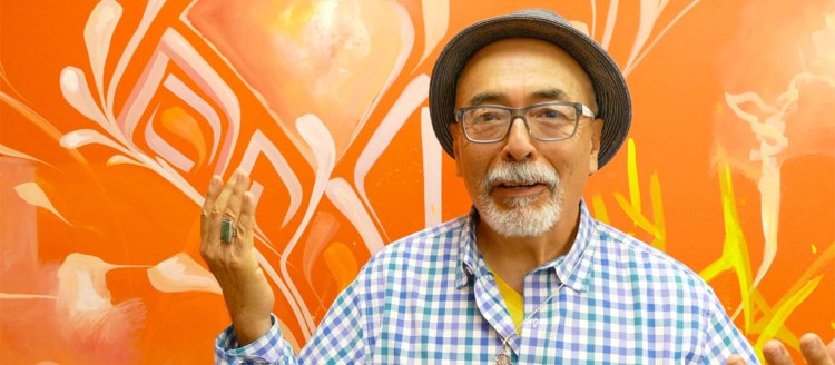 Juan Felipe Herrera in front of an orange patterned wall in the Laureate Lab Visual Wordist Studio.