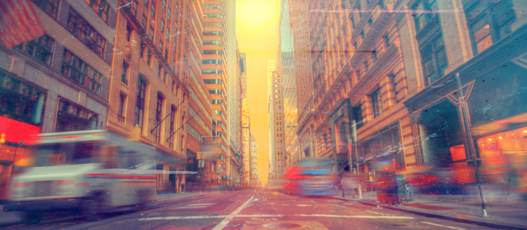 A city street in an orange sunset-like glow in perspective as objects in motion are blured.