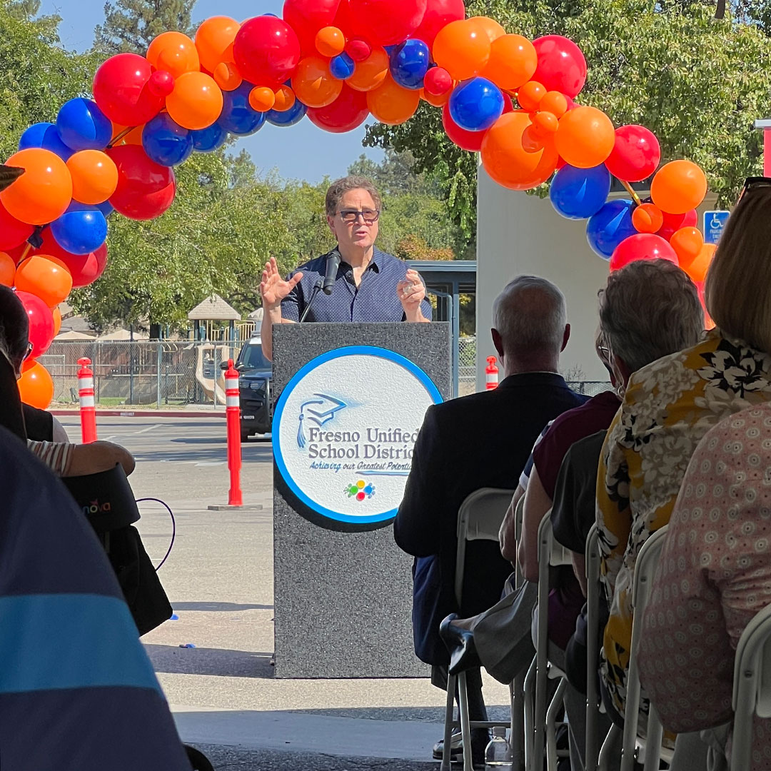 Author and Journalist Mark Arax speak at the podium with an arch of balloons.