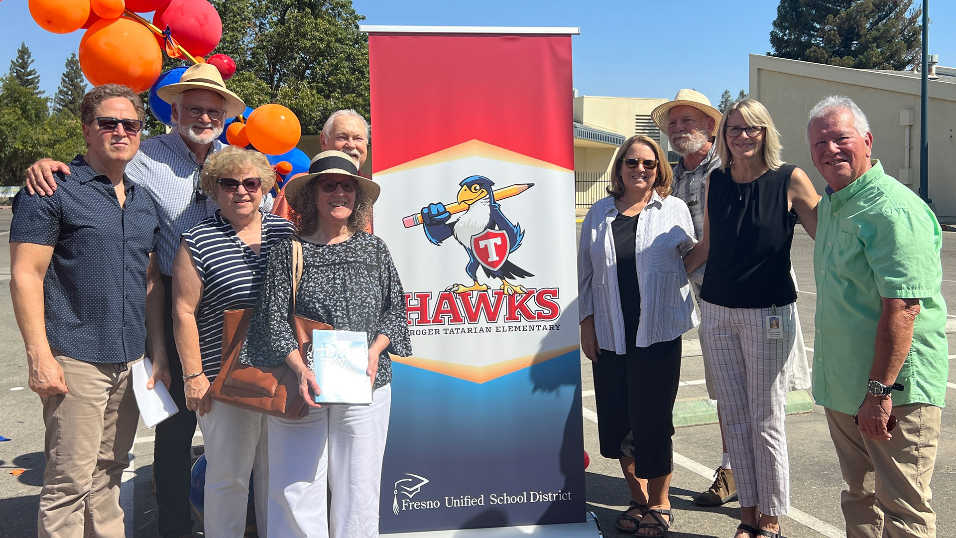 Former students of Roger Tatarian pose for a photo with the Tatarian Hawks logo