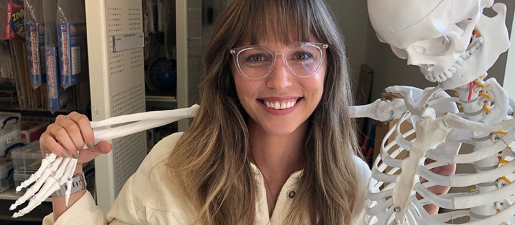 Taylor Petersen posing with a skeleton, smiling.