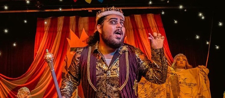 Theatre arts student in performance with a colorful, circus like background.