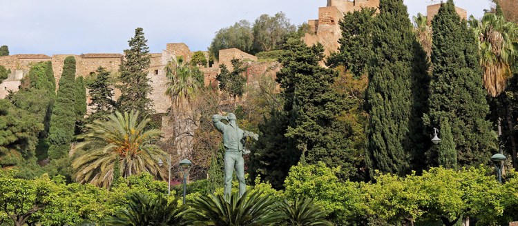 The Alcazaba of Malaga is surrounded by trees and a statue in the front.