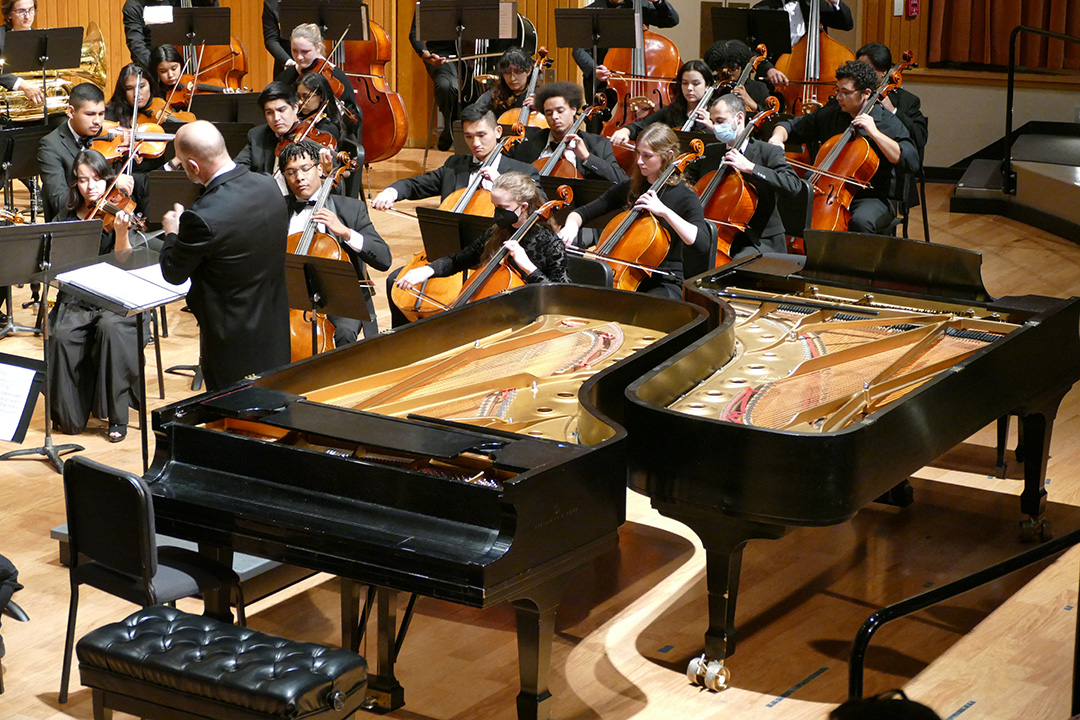 Dr. Thomas Loewenhiem conducting the orchestra with two pianos behind him.