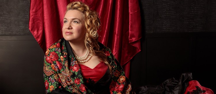Dr. Maria Briggs reclines in front of a deep red tapestry wearing a deep red dress with the flower paisley shawl.