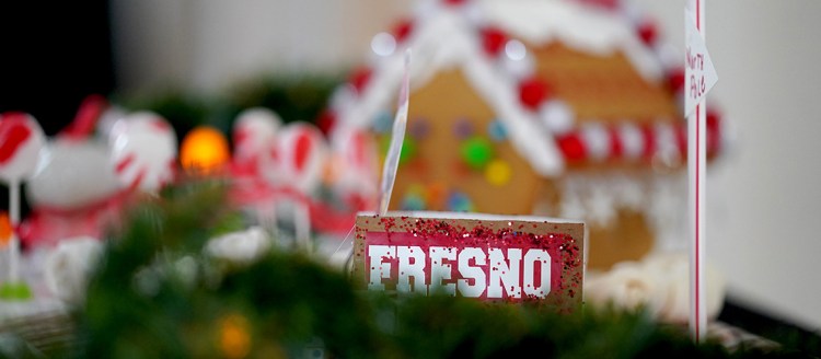 Red miniture Fresno sign next to a North Pole sign made from a drinking straw and piece of paper in front of a blurry gingerbread house.