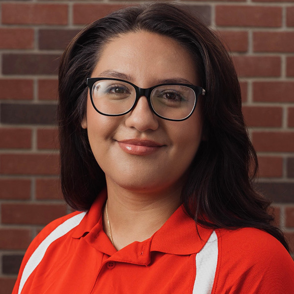 Karla Sanchez stands in front of a brick wall.