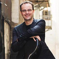 Tom Landschoot holds his cello case on a tan background.