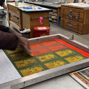 Brown is pushing the ink through the mesh to form and imprint the pattern on the bottom surface.