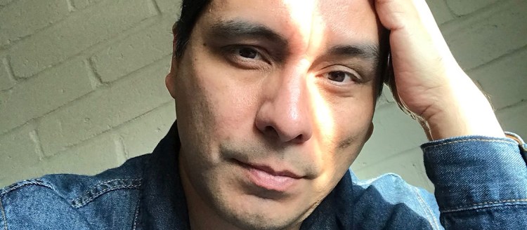 Manuel Muñoz in a blue denim jacket and left hand in his hair. Photo by Manuel Muñoz