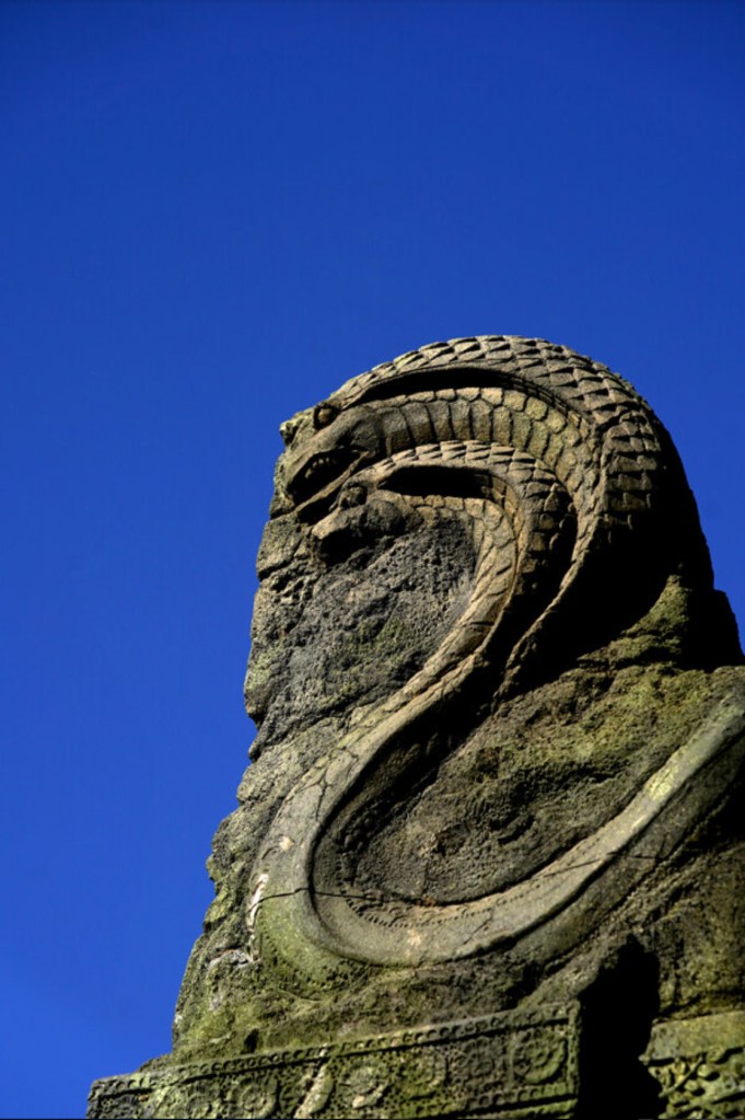 Intricate rock work depicting a serpent in stone contrasts against the blue sky.