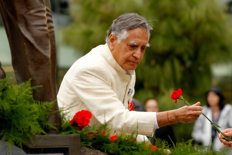 Dr. Kapoor in a white jacket lays a red flower at the feet of a statue in the Peace Garden.