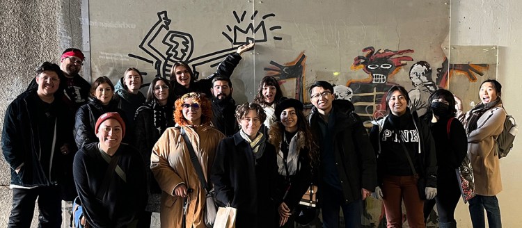 Students stand in front of "Basquiat being welcomed by the Metropolitan Police" by Banksy on the wall of the Barbican Centre.