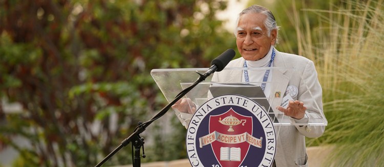 Dr. Kapoor stands at a podium at in the Peace Garden at Fresno State.