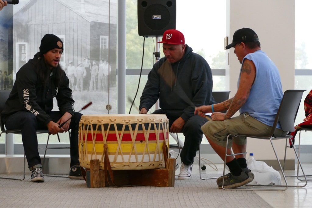 Three drummers play a single large drum providing a beat the traditional dancers.