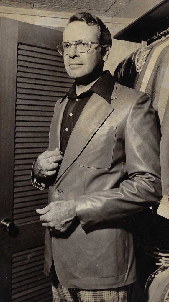 A sepia tone picture of Ralph Shabazian with a leather sport jacket and black shirt in front of his closet.
