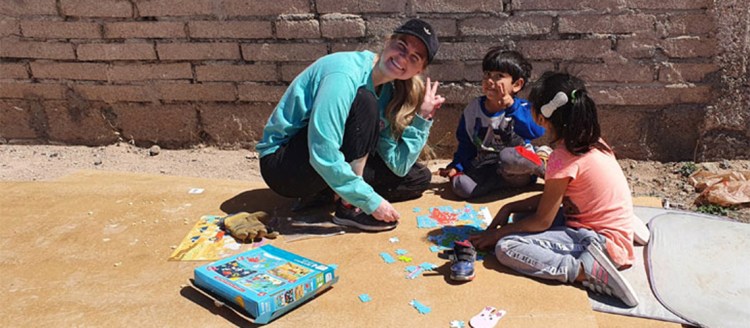 Hannah Ellsworth crouches to put together a puzzle on the ground with two young children.