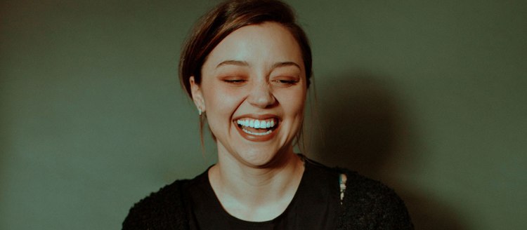 Brenna Womer with a big smile on a light green background.