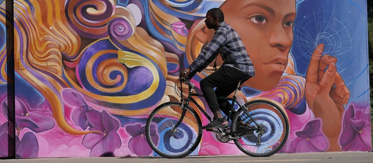 A student rides his bike in front of a large painted mural.
