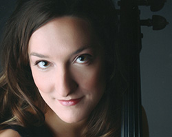 A woman looks up at the camera with only her face and top of her shoulders in frame. The left half of her face is illuminated by a bright light, while the right side of her face is in the shadows. We can see the silhouette of her cello next to the right side of her face.
