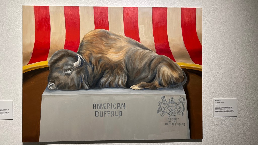 Paining of an American Buffalo, dead on a pedestal in front of an American Flag. The paining is by Idaly Rodriguez and called "The Spectacle of Conquest"