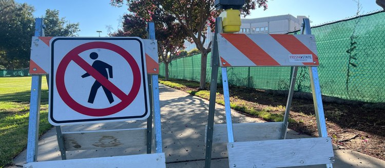 No walking signs in front of a sidewalk and construction fence.