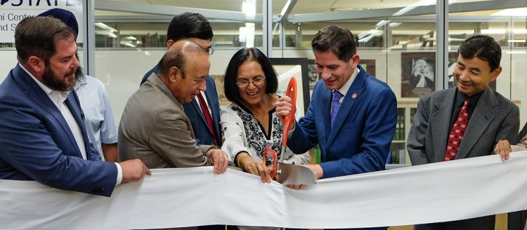 President Jiménez-Sandoval, Drs. Ravi and Naina Patel, and others stand in front of the M.K. Gandhi Center and cut a ribbon with oversized scissors.
