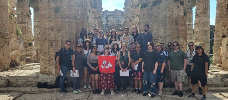 Fresno State students hold up a bulldog flag in front of ruined Roman pillars