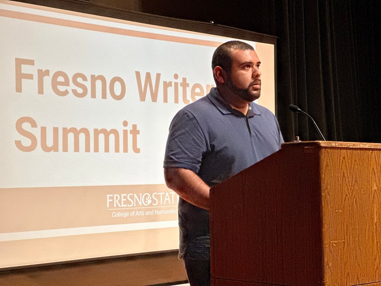 Alberto Saldaña Uribe at a podium with a presentation screen that says "Fresno Writers Summit" behind him.