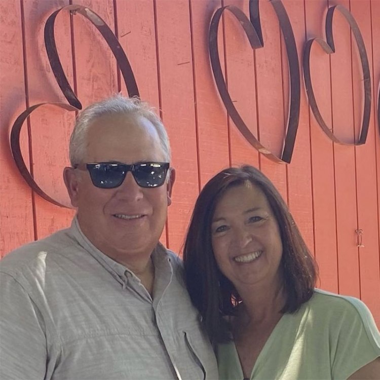 Randy and Ruth Ataíde in front of a burnt-orange wall with metal hearts.