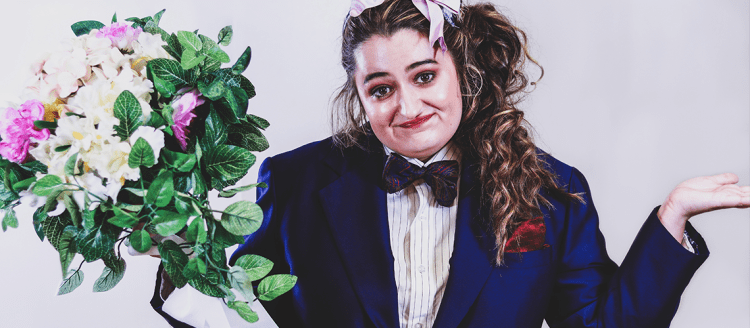 Woman in a blazer and bow tie holds a bouquet of flowers.